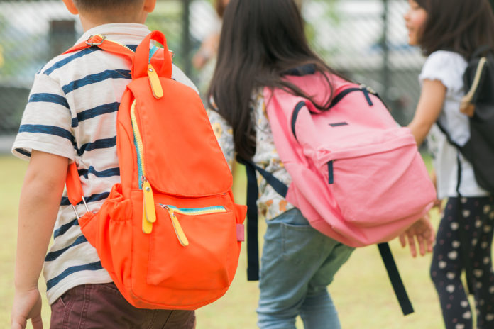 Three pupils of primary school go hand in hand. Boy and girl wit