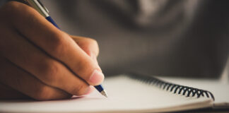 Main d'homme qui écrit avec son stylo sur un cahier