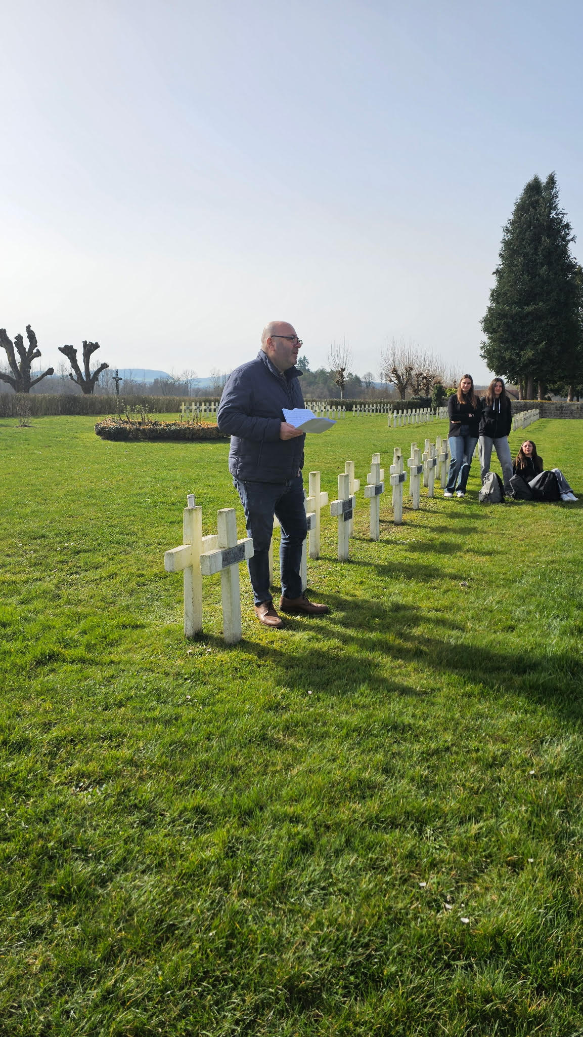 Un homme parle devant des croix dans la nécropole nationale Rougemont, entouré de lycéens, lors d
